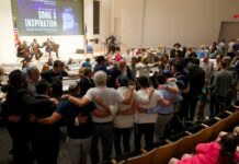 DMV Chabad Centers Honor Lubavitcher Rebbe on the 30th Anniversary of His Death Dozens of people with their arms around each other form a circle in an auditorium. In front of the people is a screen that reads "An Evening of Song & Inspiration."