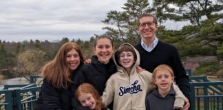 Photo of a smiling family of six: one mom, one dad, two daughters and two sons.