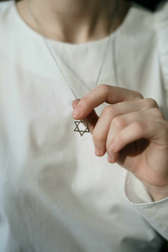 Close-up photo of a person dressed in white with one hand holding onto a silver Star of David necklace