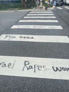 Photo of a crosswalk. The painted white lines in the road read "Israel rapes women," "Free Gaza" and "Israel rapes men."