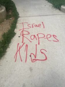 Photo of a sidewalk that has red spray-painted text that reads "Israel rapes kids."
