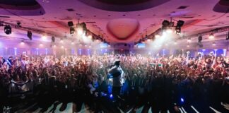 Photo of a large dance floor at night with dozens of people dancing under bright white lights.