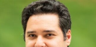 Headshot of a man with short dark hair, a suit and a red tie.