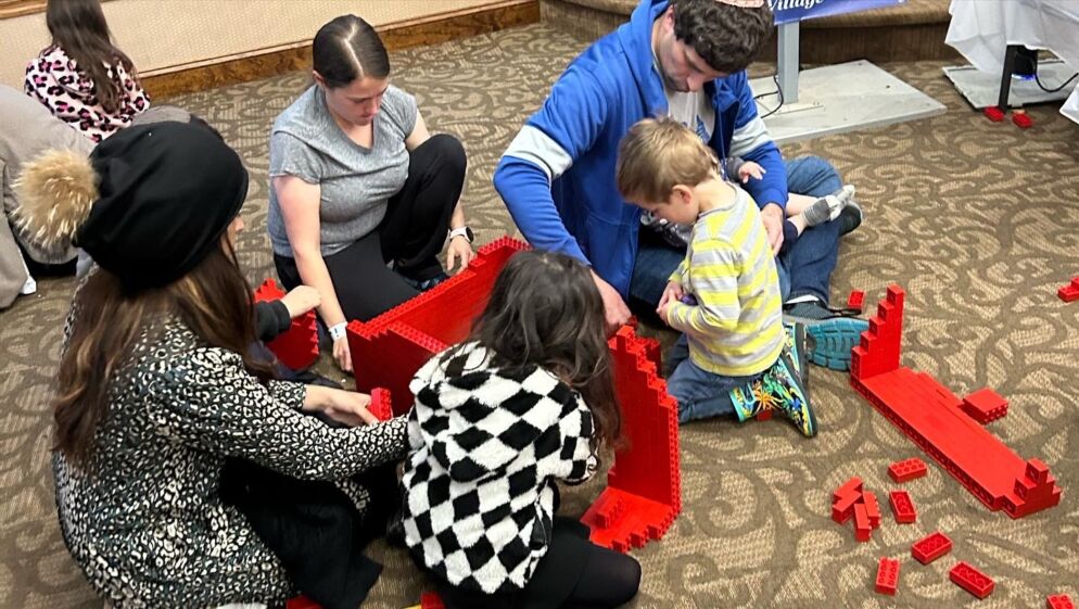 Photo of children and their families building a large structure out of red LEGO bricks.