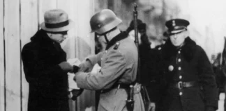 Black-and-white photo of Polish and German police officers looking at a pedestrian's papers in the street.