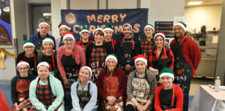 Photo of 18 young people wearing red or green Santa hats and Christmas sweaters posing for a group picture.