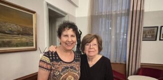 Photo of two middle-aged women with their arms around each other inside a building. They both have short brown hair.