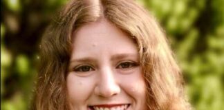 Headshot of a young woman with wavy light brown hair smiling at the camera outside.