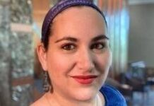 Headshot of a woman with her hair pulled back in a bandana. She is wearing a blue top and smiling at the camera.