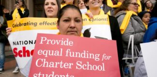 Photo of a woman at a protest holding up a red sign that reads "Provide equal funding for Charter School students."