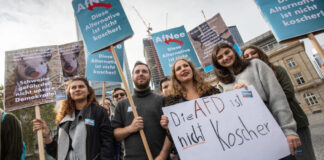 Photo of dozens of protesters holding up signs with German text written on them.