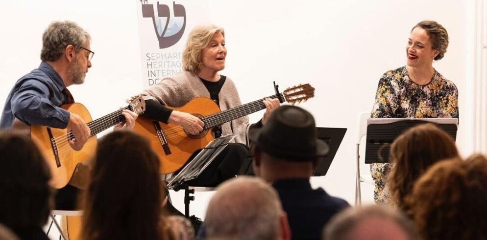 Photo of a musical trio of adults performing together. Two artists are playing acoustic guitars and another is singing.