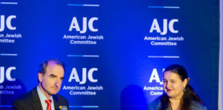 Photo of a man and a woman seated on stage with a blue banner behind them that says "AJC."