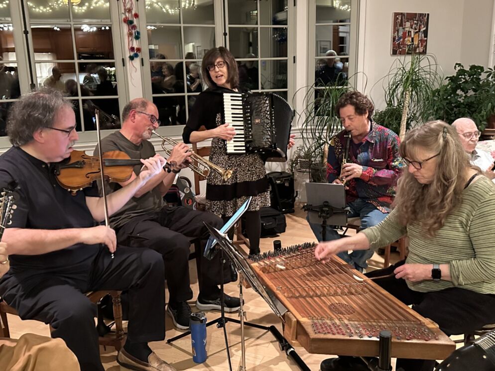 Photo of a half dozen people playing various musical instruments in a living room.