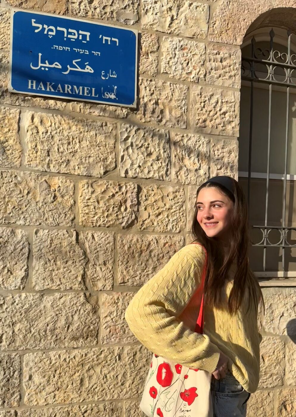 Photo of a young woman posing in front of a concrete building looking off to the side.