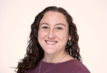 Am Kolel to Mark Lag B’Omer in the Park Headshot of a woman with curly brown hair smiling at the camera. She is wearing a purple long-sleeved shirt and a necklace.