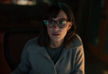 Dark photo of an actress with brown hair and glasses.