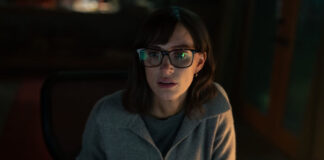 Dark photo of an actress with brown hair and glasses.