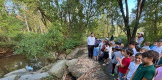 Group photo of dozens of kids standing on a riverbank with their teacher.