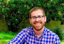 GW Hillel Announces $4M Gift to Expand Educational Programming Headshot of a man with glasses and stubble on his face wearing a blue checkered plaid shirt. He is sitting on the grass and smiling at the camera.