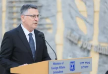 Opinion: The Responsibility of Leadership Is to Act A man wearing glasses, a jacket and blue tie speaking at a podium.