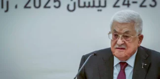 A man with white hair and a mustache, wearing glasses and a jacket and tie.