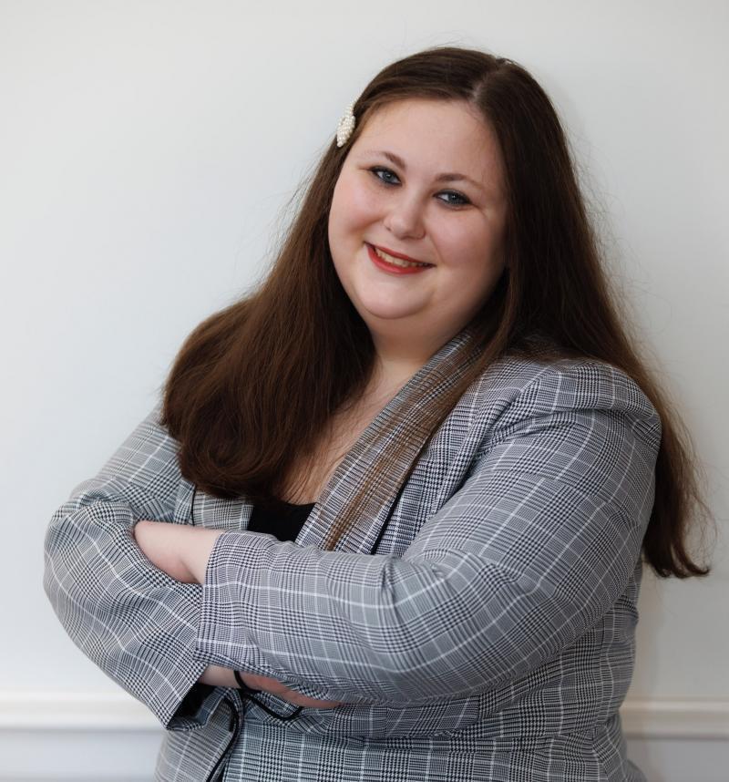 Marissa Ditkowsky, dressed in a business suit, crosses her arms and smiles in this portrait shot.