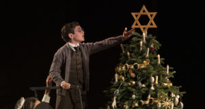 A young actor affixes a large Star of David atop a Christmas tree in the play Leopoldstadt by Tom Stoppard.