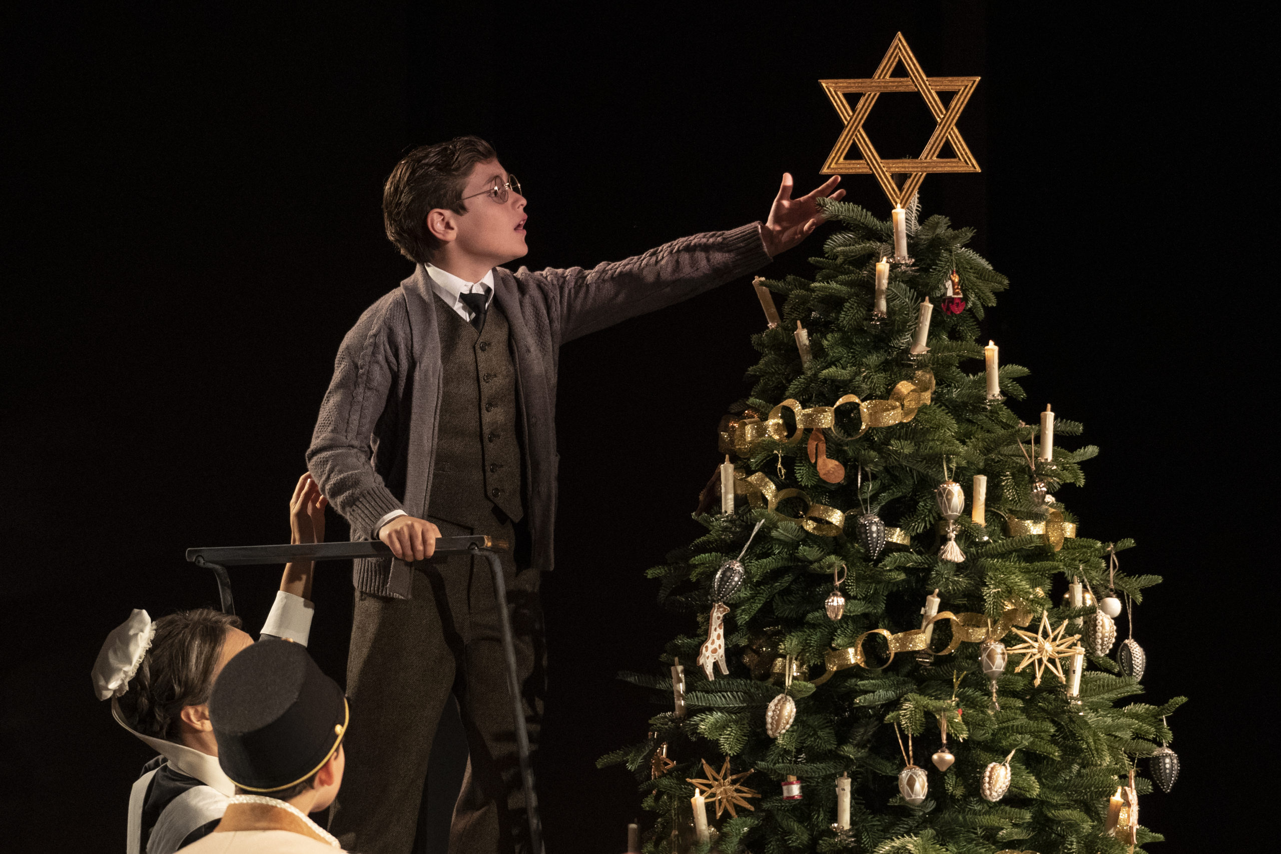A young actor affixes a large Star of David atop a Christmas tree in the play Leopoldstadt by Tom Stoppard.