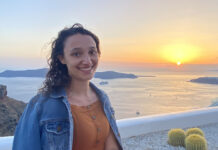 Liat Bershad Forges Community Through George Mason Hillel Photo of a young woman with curly shoulder-length brown hair at a beach. She is wearing a light brown dress with a jean jacket draped around her shoulders.