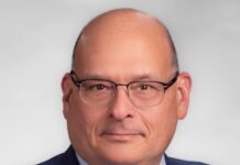 A man wearing a jacket, yellow tie and glasses.