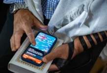 A man holding a cell phone and white prayer book.