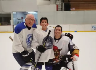 A grandfather, son and grandson wearing hockey jerseys at an ice rink.