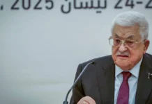 A man with white hair and a mustache, wearing glasses and a jacket and tie.