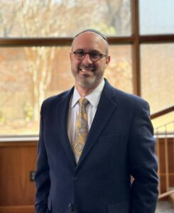 A man with glasses and a beard wearing a jacket and tie.